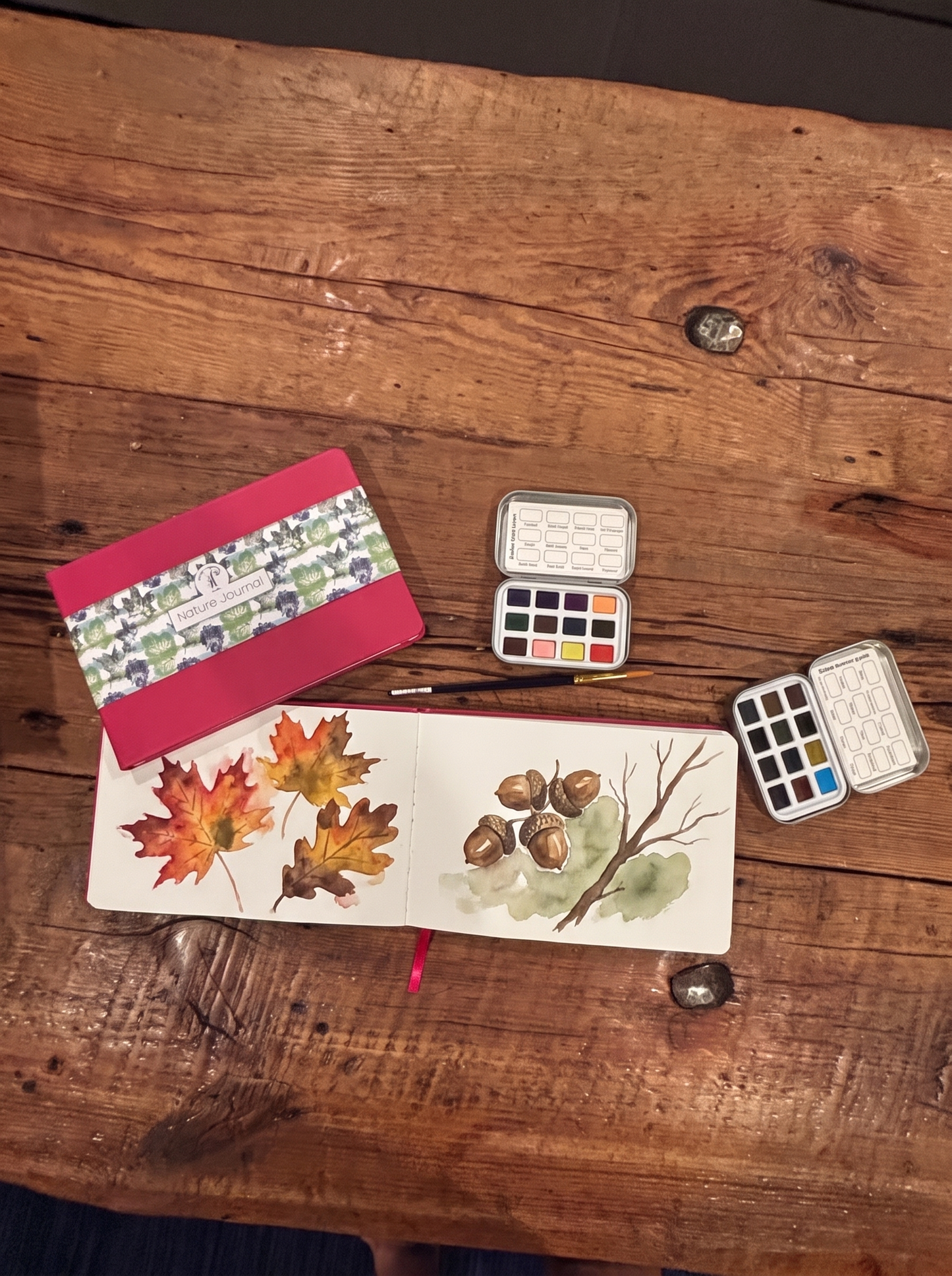 Autumn watercolor leaf and acorn studies painted in an open nature journal beside the palette tins
